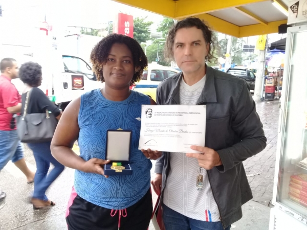 A Medalha Chico Mendes é entregue pelas mãos do docente Rafael Dias a Andreza Macedo, irmã do jovem Hiago, assassinado em Niterói 